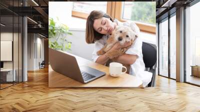 Attractive young female freelancer works on laptop from home and her cute pet dog helps her	 Wall mural