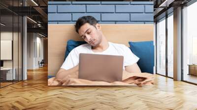 Lazy young handsome man sleeping on bed while working on laptop at home Wall mural