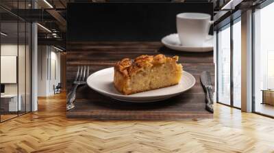 Piece of homemade traditional cornish apple pie on a white plate with a knife and fork on a wooden table. Cup of tea in the background Wall mural