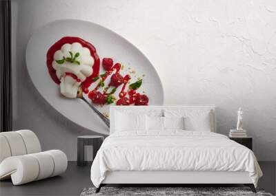 Spoon with a piece of panna cotta with syrup, raspberries and mint in oval plate, food stylind, high key, top view Wall mural