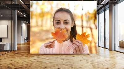 Autumn outdoor portrait of young smiling woman holding autumn leaves in autumn park with colorful leaves on fall nature background. Wall mural