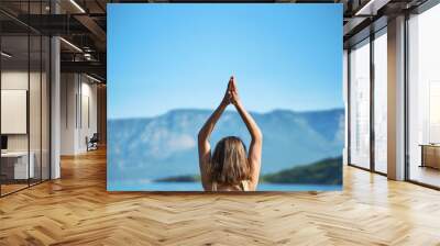 Back view woman practices yoga with hands up pose at nature with beutiful mountains view. Body and mental welness Wall mural