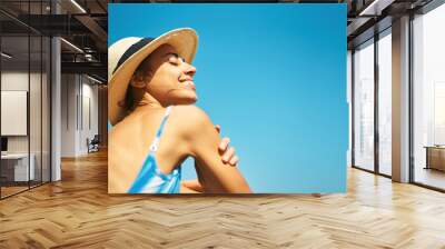 Carefree relaxed woman in hat enjoying summer beach vacation. Smiling tanned girl feeling hapiness and refreshed against bright blu sky Wall mural