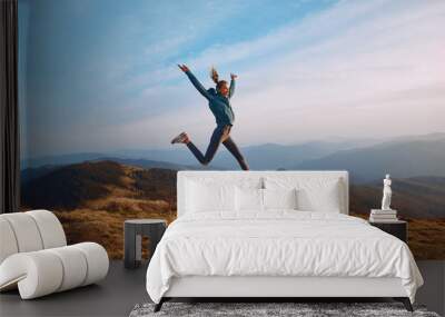 Happy woman hiker jumping on mountain ridge on blue cloudy sky and mountains background. Travel and active lifestyle concept. Wall mural