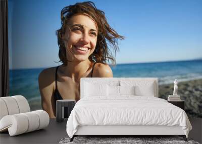 Outdoor shot of smiling young female model enjoying at sea beach against blue sky. Woman having fun out on a summer day. Wall mural