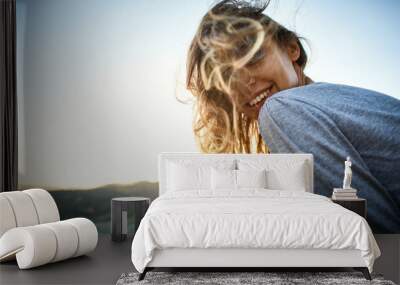 portrait of smiling cheerful woman with long hair sitting on edge of cliff against background of sunrise. woman's hair fluttering beautifully in the wind Wall mural