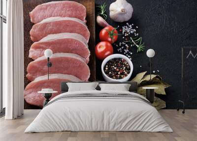 Raw sliced pork loin with tomato, pepper, rosemary, bay leaf and garlic on a dark background. Fresh meat. Wall mural