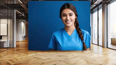 Portrait of a smiling female doctor or nurse wearing blue scrubs uniform on blue background. Wall mural