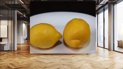 Close-up image. Still life with two ripe bright yellow lemons lying on a white serving plate standing on a table with a dark background Wall mural