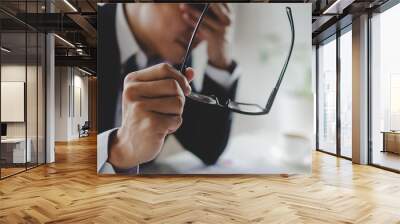 tired asian young businessman feeling stressed and taking off eyeglasses feels eye strain fatigue after long office work on computer, overwork, office syndrome, business problem and financial concept Wall mural