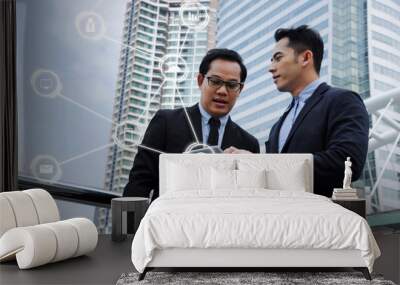 two business asian handome man talking and reading information about finance news in mobile tablet together standing in modern city with icon network, investment, technology, internet concept Wall mural