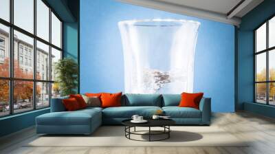 Transparent glass with water inside on blue background Wall mural