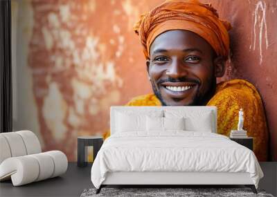 A handsome Malian man. Mali. A joyful man in traditional attire with a vibrant orange headwrap smiles warmly against a textured rust-colored wall, showcasing cultural pride and happiness. . #motw Wall mural