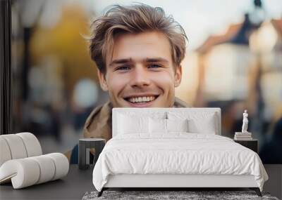 A handsome Swedish man. Sweden. A cheerful young man with tousled hair smiles warmly at the camera, set against a blurred urban background that suggests a vibrant outdoor scene. . #motw Wall mural