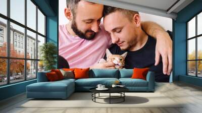 Gay couple playing with kitten. Wall mural