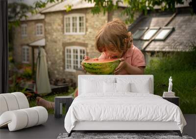 A little toddler boy is eating fresh watermelon on a sunny day on his summer holidays at the countryside in a cottage in England Wall mural