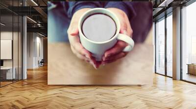 A woman's hand holding a coffee cup on a wooden table top view Wall mural