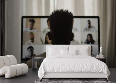 A rear view of a person participating in a virtual conference on a desktop monitor, symbolizing remote work and digital connectivity. Wall mural