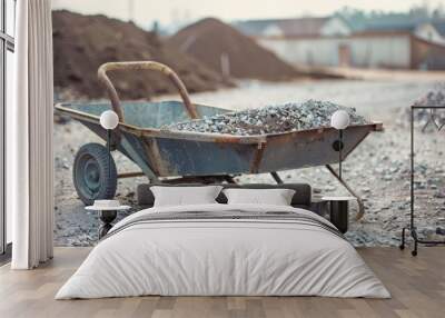 A weathered wheelbarrow filled with gravel on a construction site, reflecting the labor and hard work involved in building. Wall mural