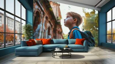 A young boy, captivated by his surroundings, looks up in wonder at an ancient stone structure bathed in the warm glow of the setting sun. Wall mural