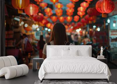 A young woman with a backpack explores a bustling street market adorned with vibrant red lanterns, immersing herself in the lively evening ambiance. Wall mural