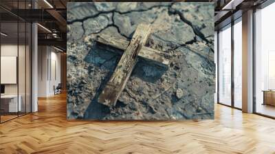 An old wooden cross lying on cracked dry ground signifies abandonment, resilience, and spiritual symbolism in a harsh environment. Wall mural