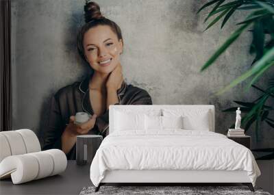 Beautiful caucasian woman in silk pajama with face cream smiling at camera Wall mural