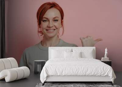 Cheerful redhead woman with happy facial expression indicating with finger at blank copy space Wall mural