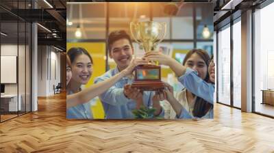 Colleagues celebrate a team achievement, lifting a golden trophy together, their faces beaming with pride and excitement in a bright, modern office setting. Wall mural