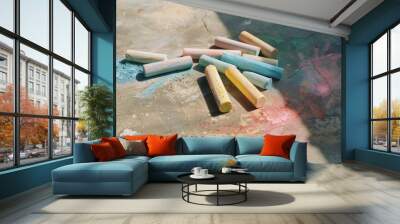 Colorful pastel chalks scattered on a concrete surface, partially shadowed, creating an artistic and playful scene. Wall mural