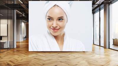 Day spa, beauty and freshness concept. Pensive European woman with healthy skin concentrated aside thoughtfully, feels refreshed after bath procedures, dressed in dressing gown, towel on head Wall mural