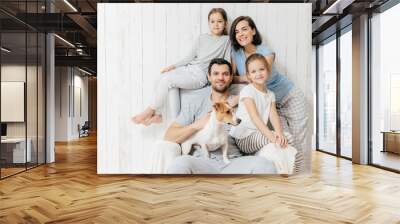 Family portrait. Happy parents with their two daughters and dog pose together against white background, spend free time at home, being in good mood. Mother, father and small sisters pose indoor Wall mural