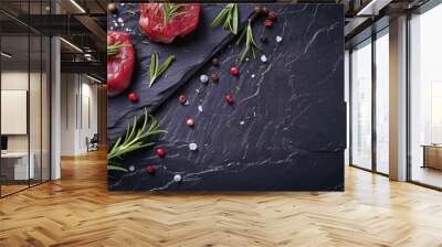 Fresh raw steaks garnished with rosemary and various spices are artfully arranged on a dark slate surface. Wall mural