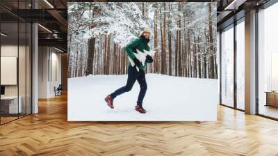 Joyful man in winter attire playfully running in a snow-covered forest, exuding happiness Wall mural