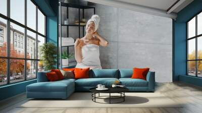 Relaxed young Caucasian female model wears towel wrapped on head, feels refreshed after taking shower, has healthy clean soft skin, poses in cozy bathroom. Women, beauty and hygiene concept. Wall mural