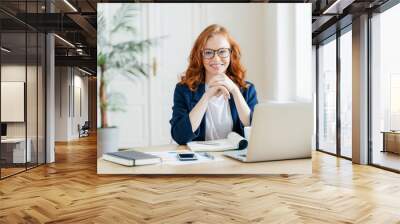 Smiling redhead woman with glasses working on a laptop at a bright home office Wall mural