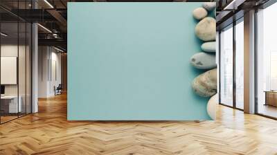 Smooth zen stones of varying sizes and colors are neatly arranged against a soothing teal background, offering a sense of balance and tranquility. Wall mural