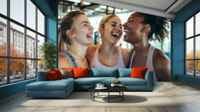 Three diverse, joyful women embracing at the gym, celebrating friendship. Wall mural