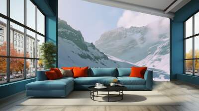 Two adventurous skiers glide down a pristine, sunlit snowy slope, framed by majestic, rugged mountains and wisps of clouds against a clear sky. Wall mural