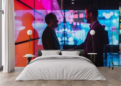 Two business professionals shake hands in a modern setting with vivid, colorful digital screens in the background. Wall mural