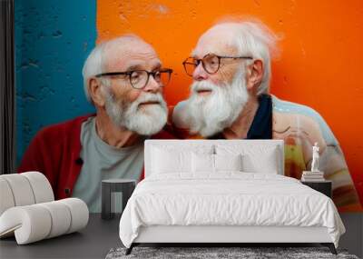 Two elderly men with white beards and glasses share a moment of camaraderie against a vibrant orange and blue backdrop. Wall mural