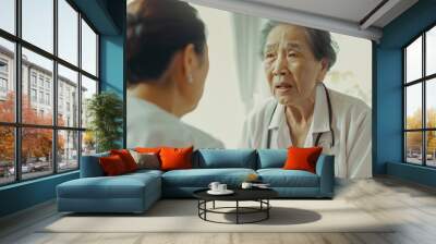 Two elderly women in medical uniforms engage in a thoughtful conversation inside a bright, softly lit room. Wall mural