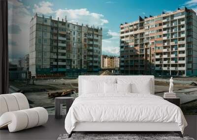 Two tall apartment buildings under construction, standing against a bright blue sky, with scattered building materials on the ground. Wall mural