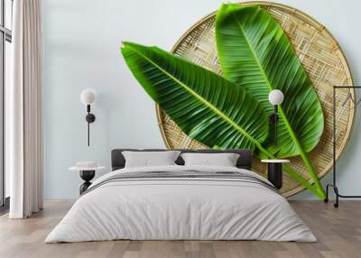 Two vibrant green banana leaves rest artistically on a wicker tray against a light background, evoking a tropical feel. Wall mural