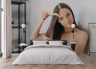 Woman brushes hair with comb after taking shower and applying hair care mask Wall mural