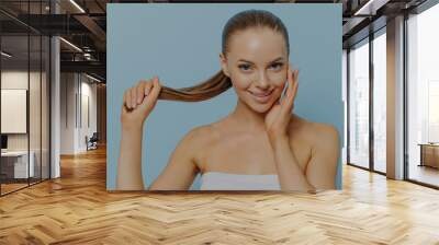 Young naturally pretty woman showing healthy-looking hair and touching clean glowing skin Wall mural