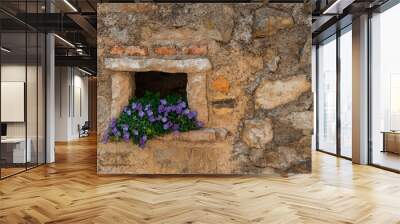 Closeup shot of a blooming purple flower bush in a hole on a stone wall Wall mural