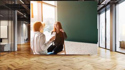 Young women talking in a cafe. Female models drinking coffee and laughing. Wall mural