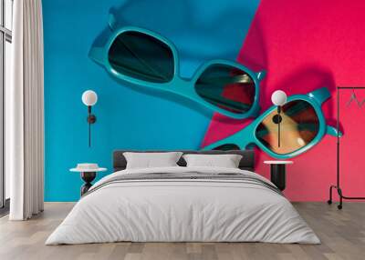 On bright pink background lie sunglasses in plastic blue frame with dark glasses. Summer. Accessories. Wall mural