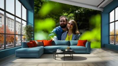 The young and modern loving couple sits among greens in the park. positive emotions. Happiness. Family. Wall mural